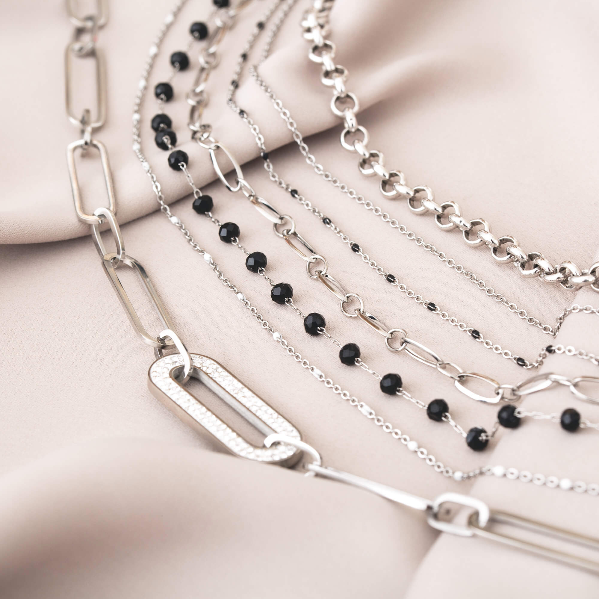 Colliers en argent et perles noires disposés sur un tissu beige satiné