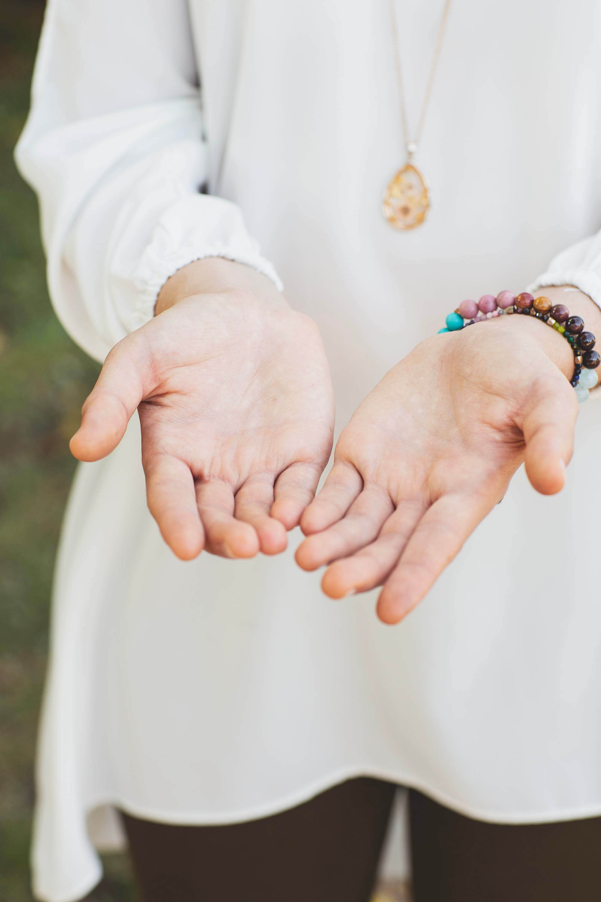 Mains ouvertes d’une femme en blouse blanche, portant des bracelets et un pendentif