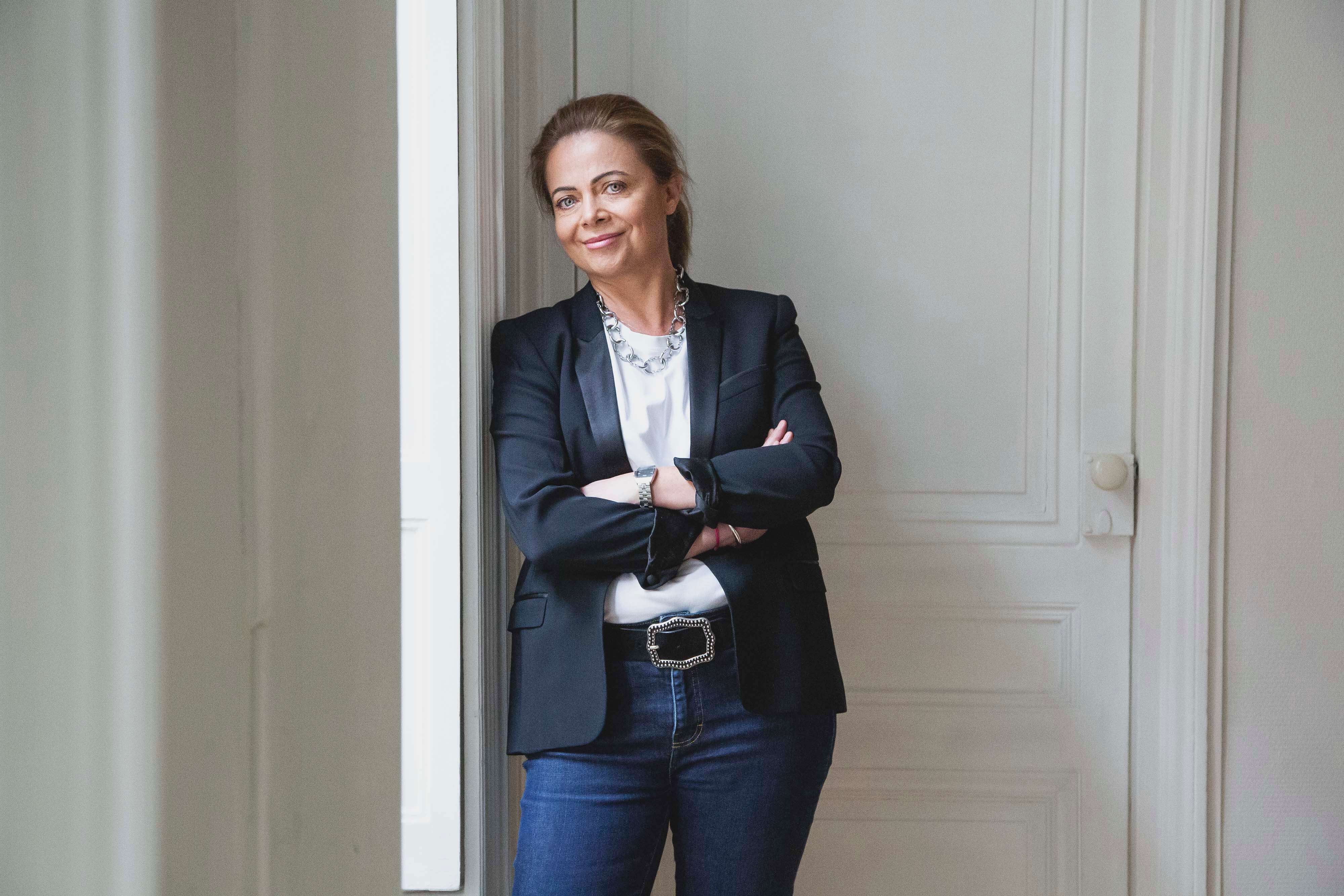 Portrait d’une femme en tailleur posant contre un mur blanc